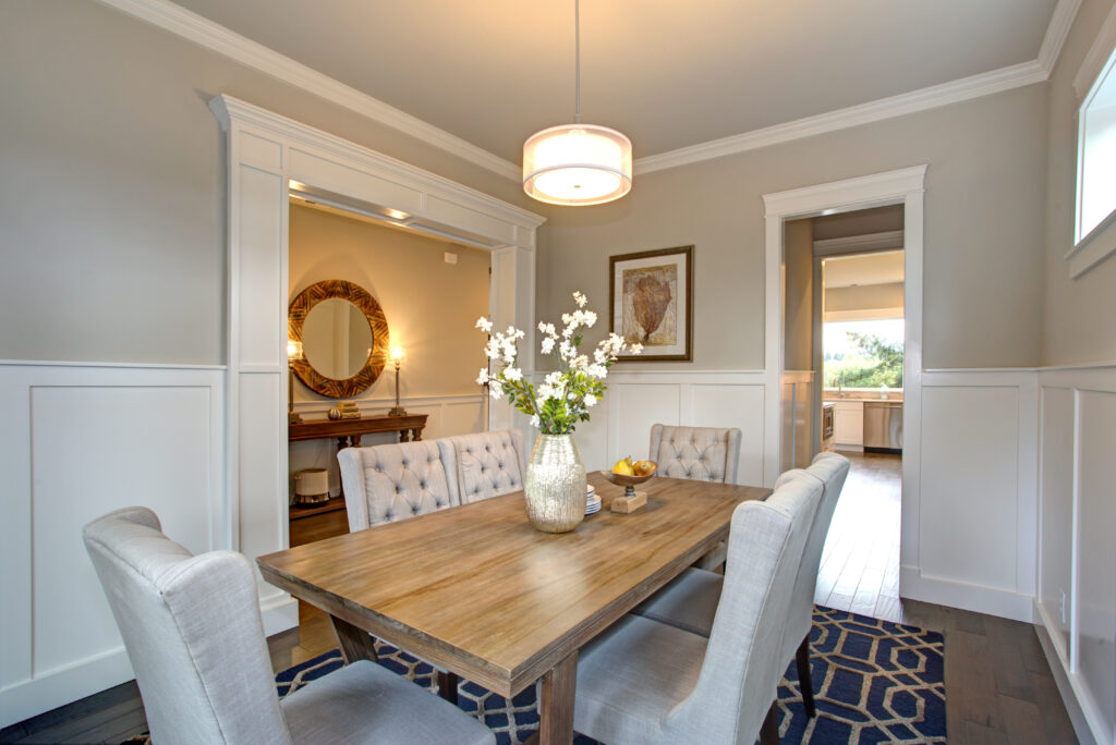 Elegant transitional dining room with board and batten walls, wood dining table surrounded by grey upholstered dining chairs.